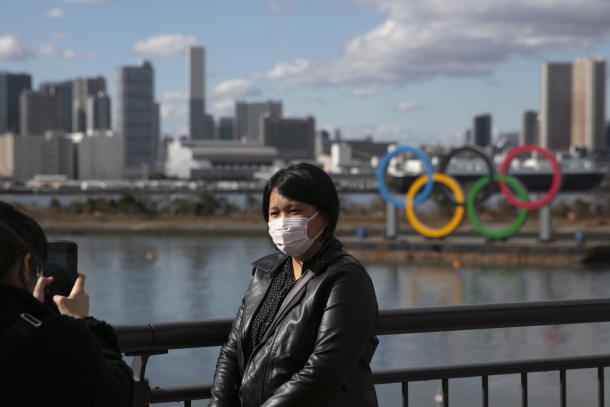 urista com máscara posa para foto em frente aos anéis olímpicos na Baía de Tóquio, no Japão 